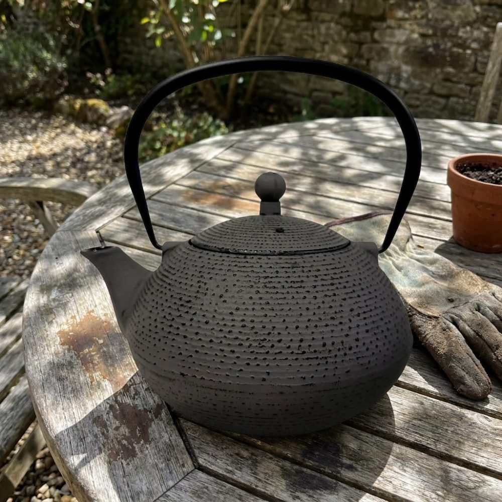 Théière en fonte 850 ml — gris anthracite, intérieur émaillé, sur une table de jardin en teck
