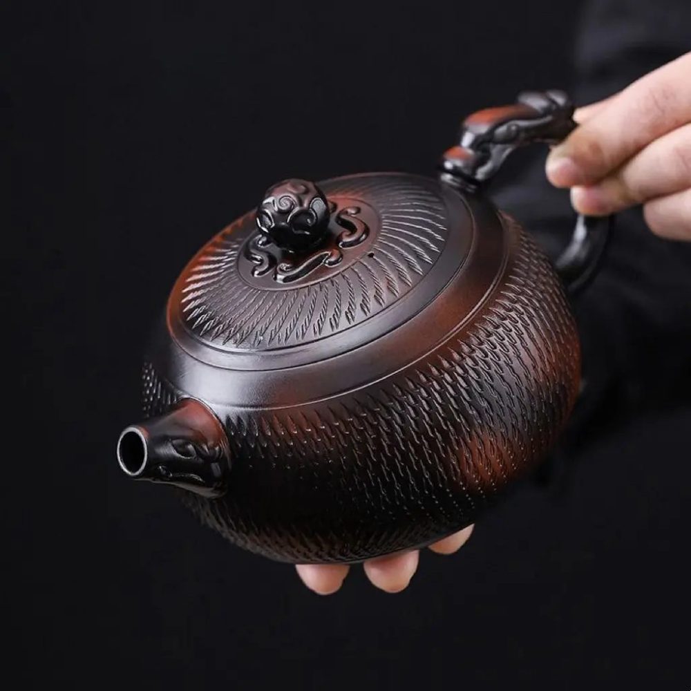 La théière tenue en main, vue de dessus : couvercle peigné et bouton sculpté