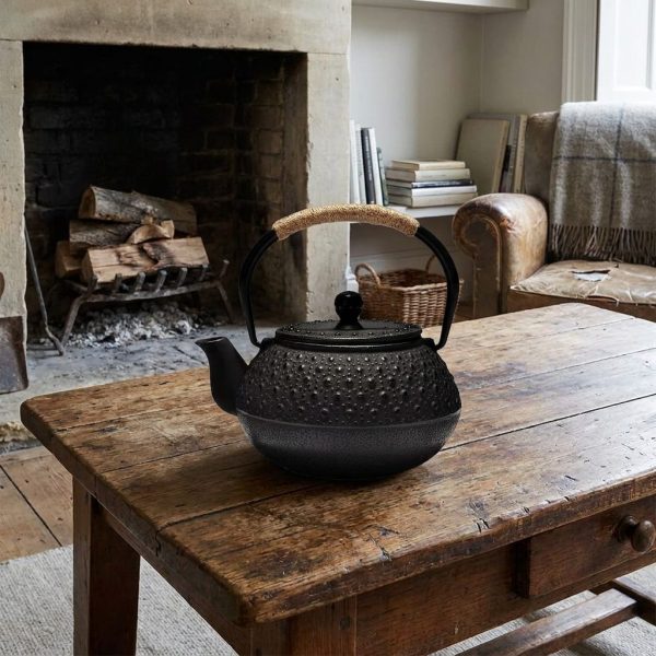 Théière en fonte 900 ml à picots arare noirs, sur une table basse en bois brut, devant une cheminée