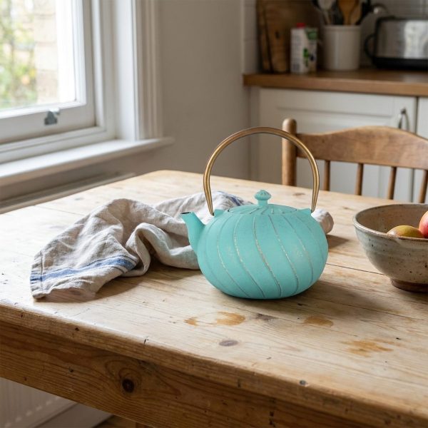 Théière en fonte émaillée 1,2 litre, turquoise à cannelures torsadées, sur une table de cuisine en bois clair, au matin